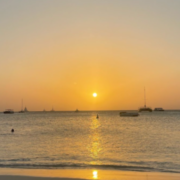 Golden sunset over the ocean at Palm Beach, Aruba, with boats on the horizon and gentle waves near shore.
