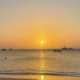 Golden sunset over the ocean at Palm Beach, Aruba, with boats on the horizon and gentle waves near shore.